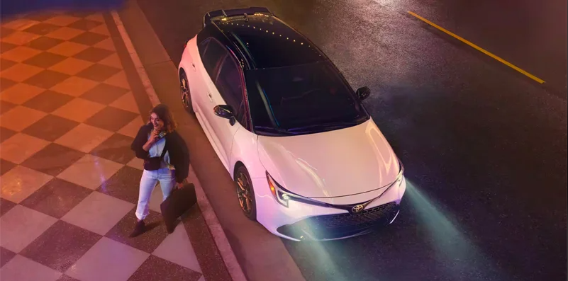 A woman climbing out of a white 2024 Toyota Corolla Hatchback.
