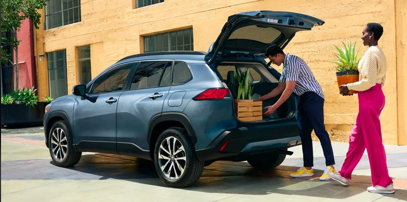 Two individuals loading potted plants in to the back of a 2024 Toyota Corolla Cross Hybrid.