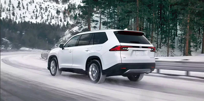 A white 2024 Toyota Grand Highlander driving down a snowy road.