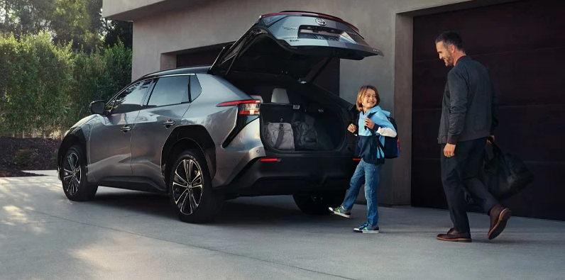 A father and his daughter walking toward the back of a 2025 Toyota bZ4X to put their bags away.