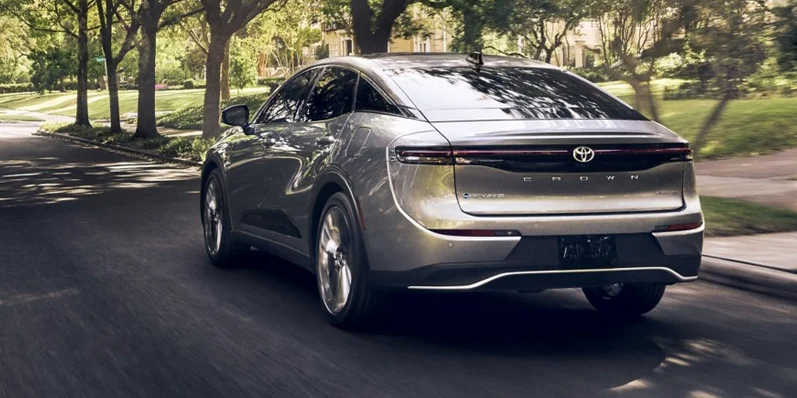 A silver 2025 Toyota Crown driving down a tree lined road.
