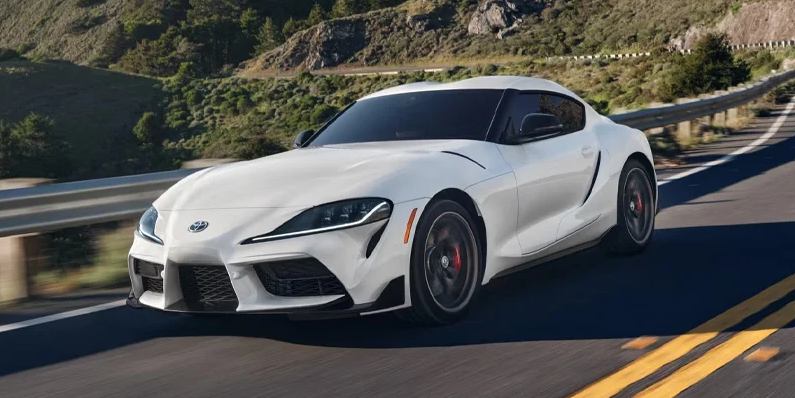 A white 2025 Toyota GR Supra driving down the road.