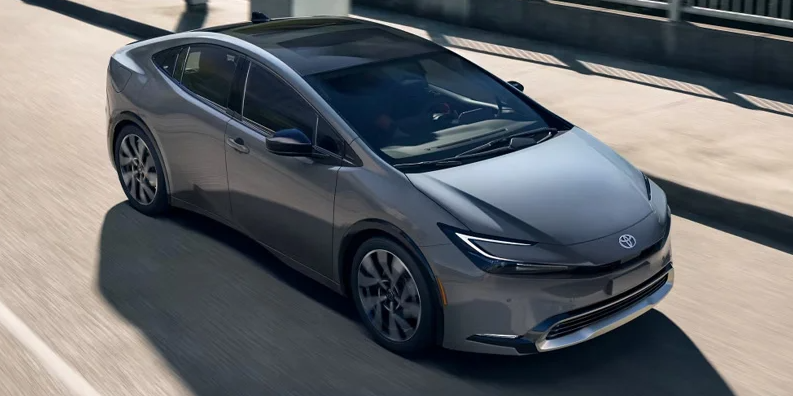 A photo of a silver 2025 Toyota Prius Plug-in Hybrid driving down the road.