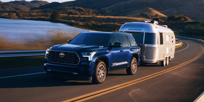 A photo of a blue 2025 Toyota Sequoia towing a camper.