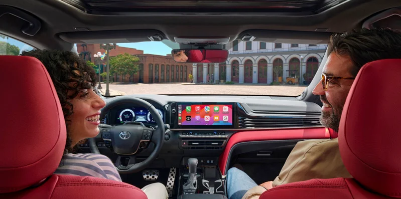 A photo of two individuals talking to each other while driving a 2025 Toyota Camry.