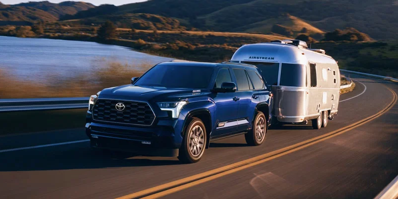 A blue 2025 Toyota Sequoia towing a camper down the road.