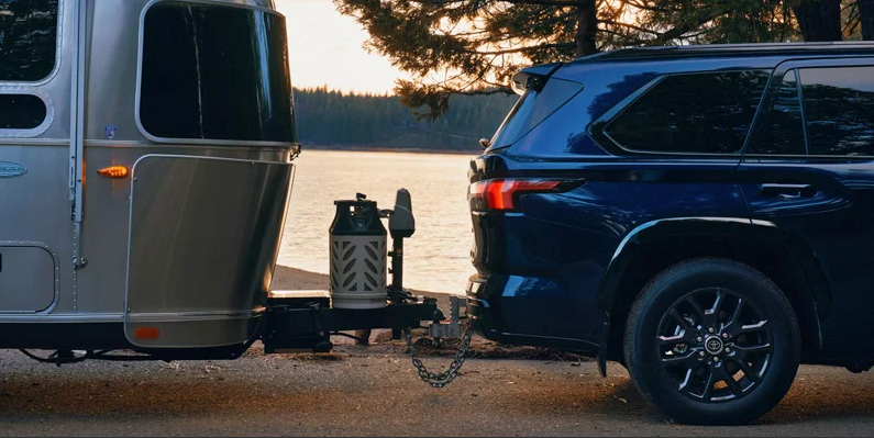 A photo of a 2025 Toyota Sequoia towing a camper near a lake.