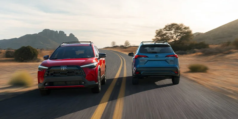 A red and blue 2026 Toyota Corolla Cross driving passed each other on the road.