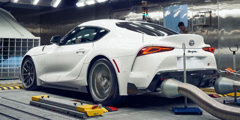 A white 2026 Toyota GR Supra undergoing performance testing on a dynamometer inside a controlled environment.