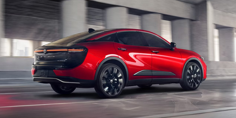 Red 2026 Toyota Crown driving through a modern urban roadway